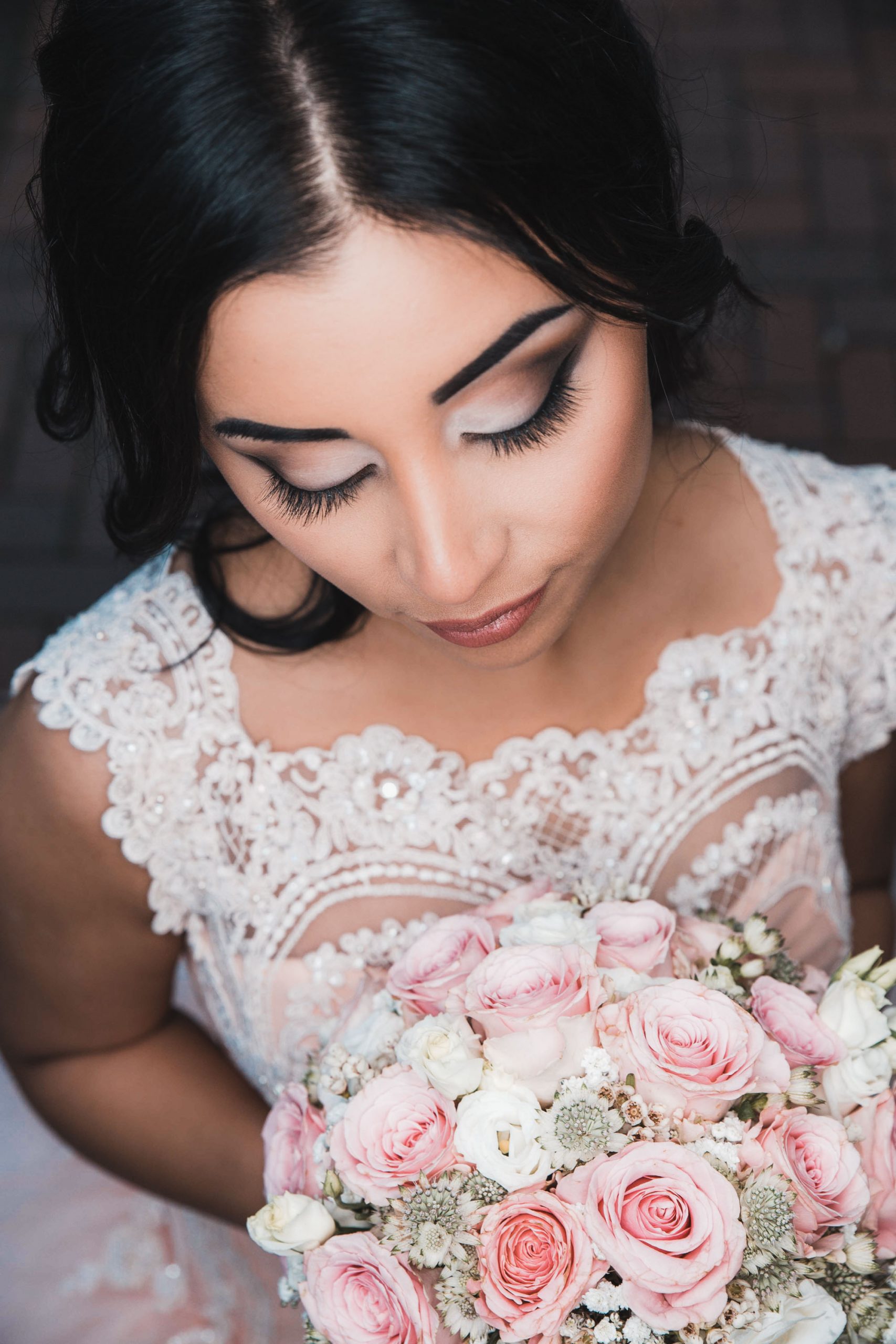 Hochzeitsbild einer schönen Braut mit perfektem Braut Styling und Brautfrisur. Hochzeitsfoto aus erhöhter Perspektive. Braut schaut verträumt auf ihren Brautstrauß.