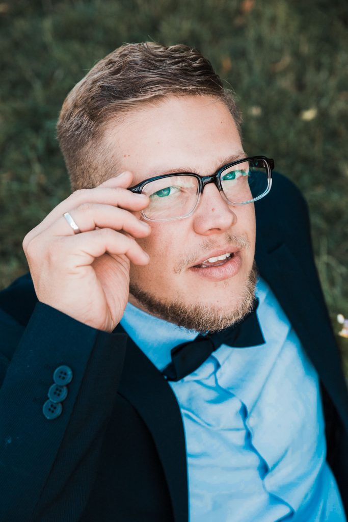 Hochzeitsbild vom Bräutigam aus erhöhter Perspektive. Bräutigam richtet seine Brille und schaut dabei in die Kamera. Kreatives Hochzeitsfoto mit Ringlicht im Einsatz.