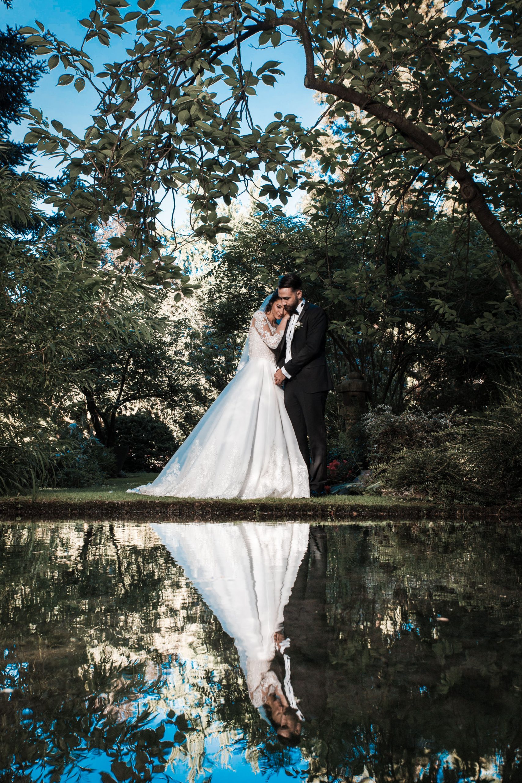 Hochzeitsbild eines türkischen Brautpaares am Wasser im japanischen Garten Leverkusen. Brautpaar spiegelt sich im Wasser. kreatives Hochzeitsfoto.