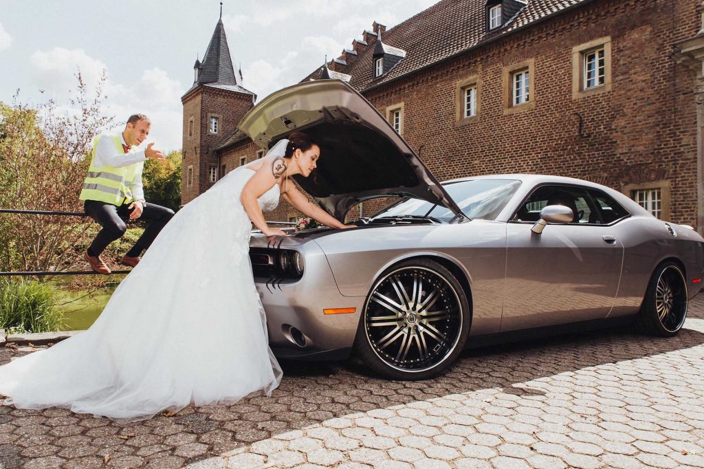 Brautpaar hat eine Autopanne, hilft da eine Hochzeitsversicherung? Lustiges Spaßfoto, diente nur zur Unterhaltung. Bräutigam steht neben dem Dodge Challenger Hellcat.