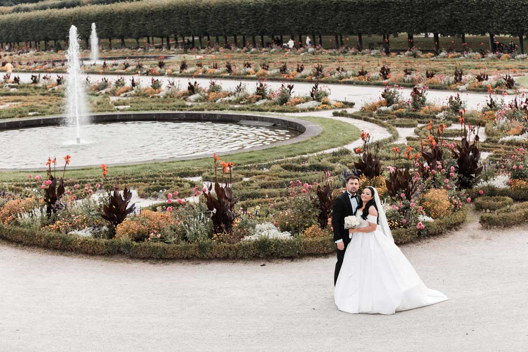Brautpaar posiert vor dem Garten des Schlossparks. Hochjzeitsbild im Weitwinkel auifgenommen, aus erhöhter Perspektive