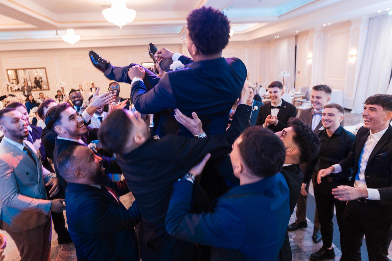 Ein somalischer Bräutigam wird von seinen Bestmen in die Luft geworfen, während im Hintergrund andere Gäste sich bei einer Hochzeit im Event Palast Hürth amüsieren.