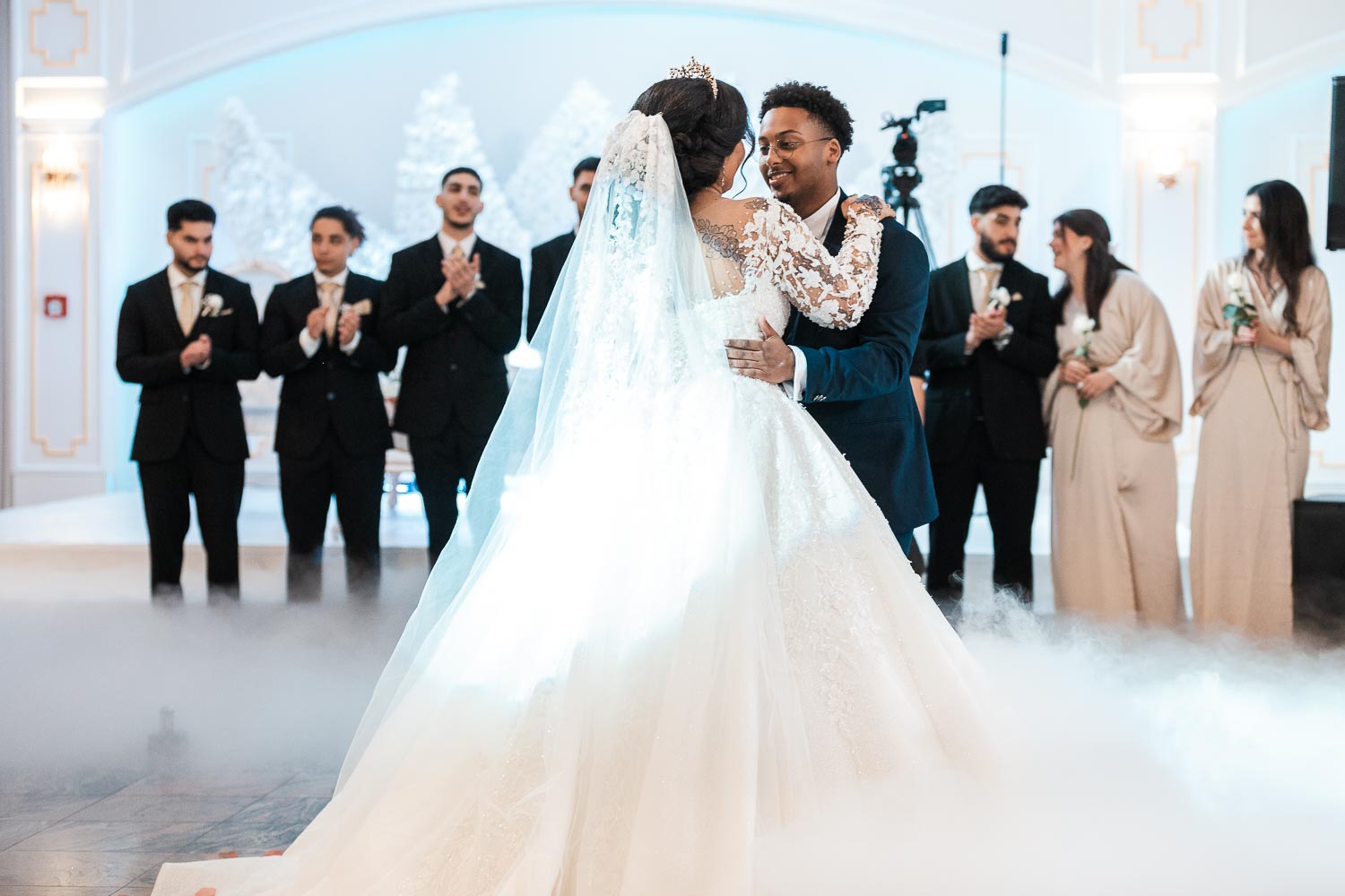Brautpaar tanzend in Umarmung, umgeben von Nebel und Feuerwerk, mit Best Men und Bridesmaids im Hintergrund.