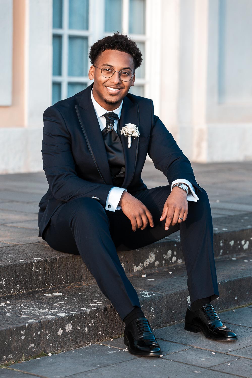 Portrait von einem somalischer Bräutigam sitzt auf den Stufen vor dem Schloss Augustusburg und blickt mit seinem strahlend weißen Lächeln in die Kamera.