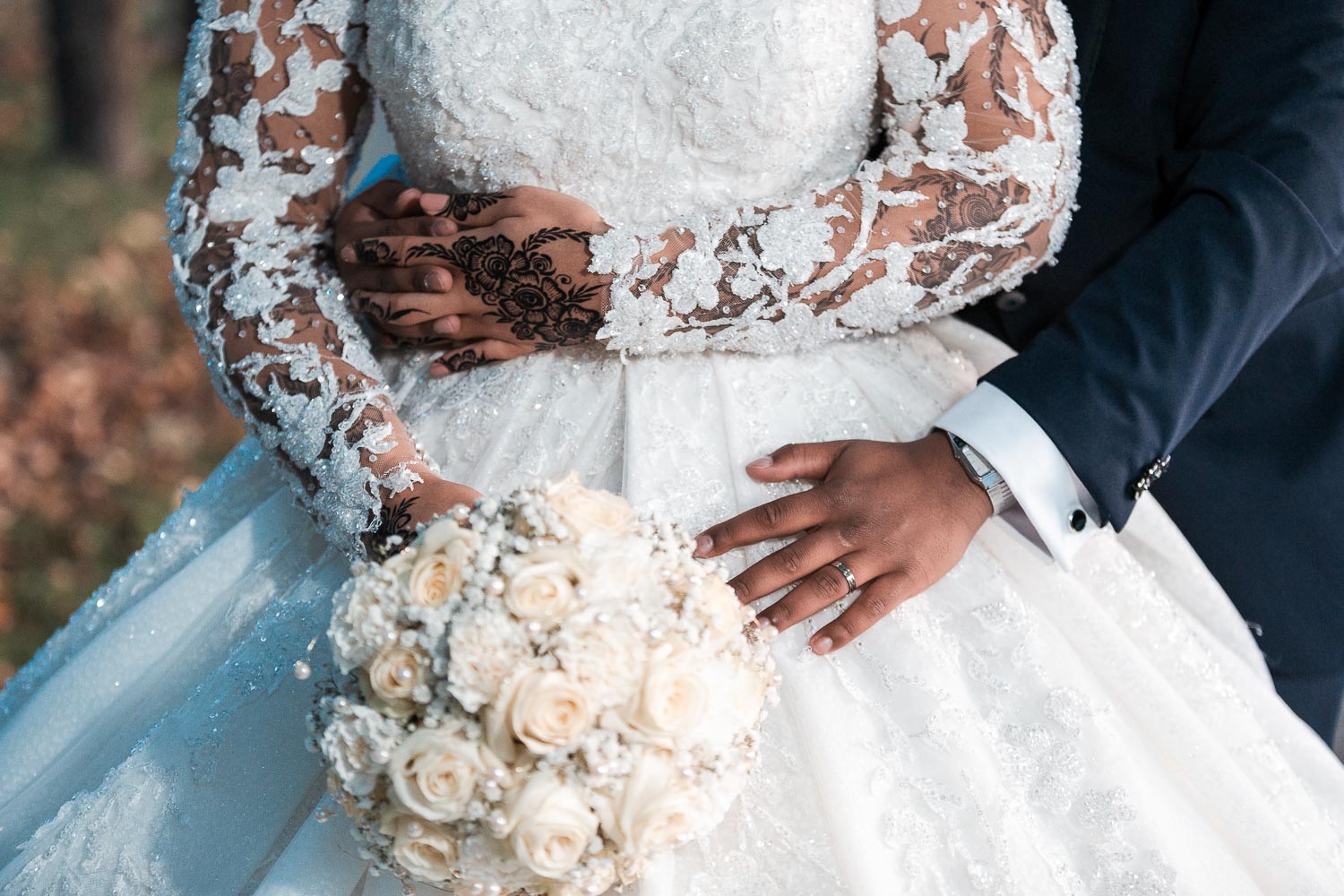 Der Bräutigam umarmt die Braut von hinten. Das Hochzeitsfoto ist unterhalb der Brust bis zur Hüfte angeschnitten und zeigt nur die Details des Kleides, von Hannah Tattoo, vom Braut Strauß, und Brautkleid und Anzug.