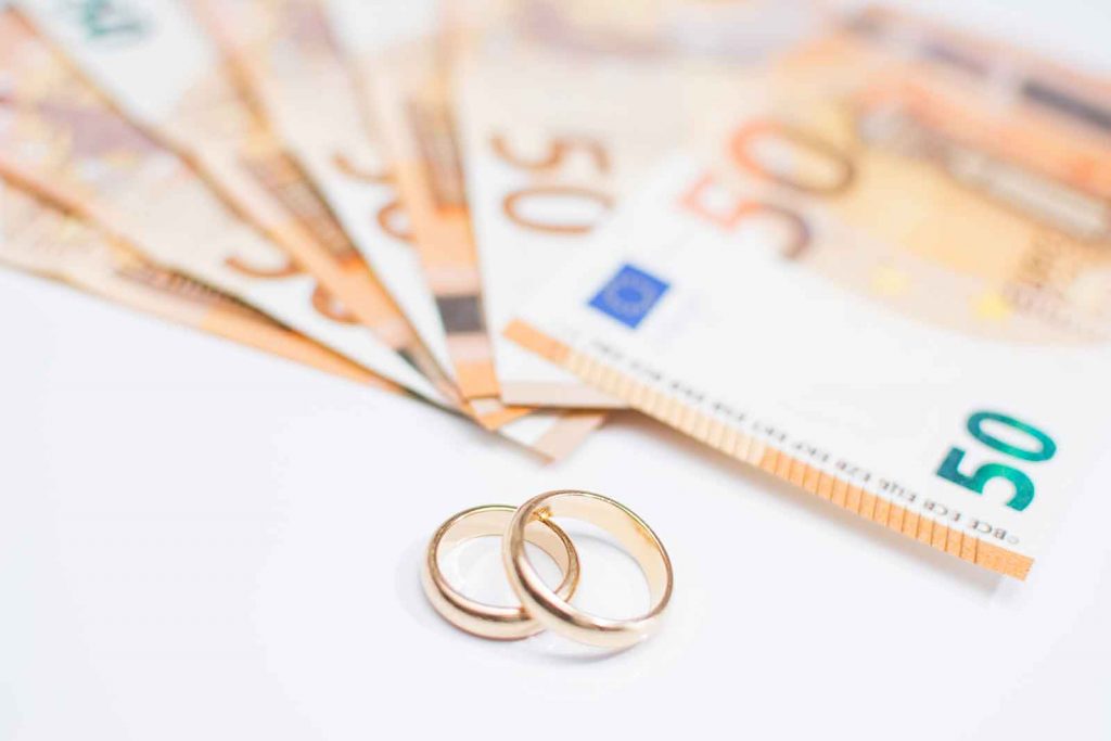 Fünfzig Euro Scheine 50€ auf einem weißen Tisch mit Eheringen die das Hochzeitsbudget darstellen