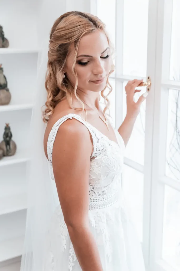Braut im Hochzeitskleid am Fenster bei einem natürlichen Porträt vor der Trauung