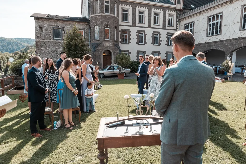Bräutigam und Hochzeitsgäste bei der freien Trauung im Außenbereich von Schloss Burgbrohl