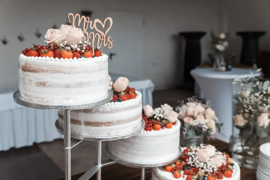 Mehrstöckige Hochzeitstorte mit Beeren, Rosen und Mr-&-Mrs-Dekoration bei der Hochzeitsfeier
