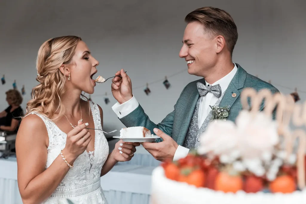 Bräutigam gibt der Braut ein Stück Hochzeitstorte bei der gemeinsamen Hochzeitsfeier