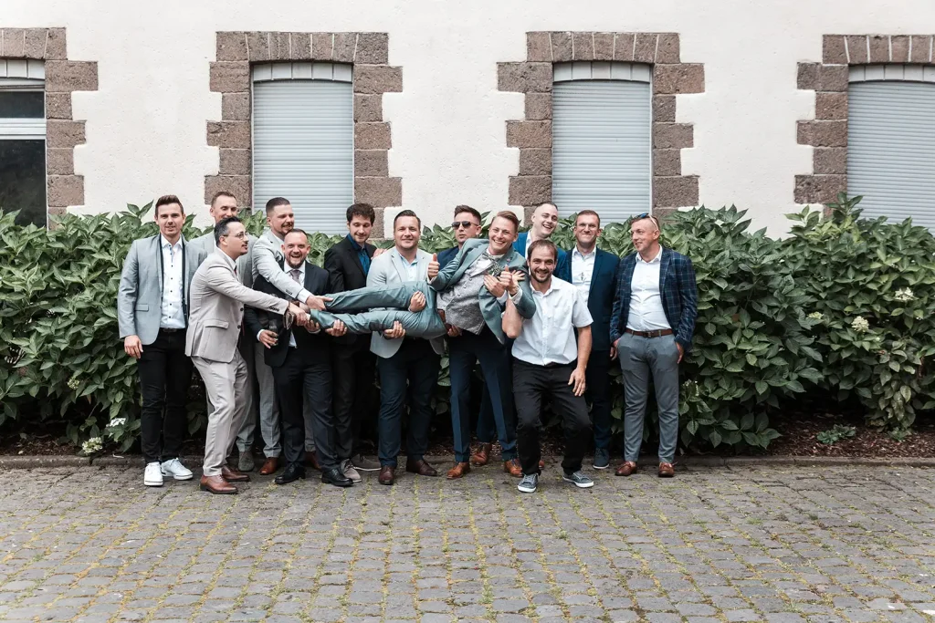 Bräutigam wird von seinen Freunden bei einem lockeren Gruppenfoto während der Hochzeit hochgehoben