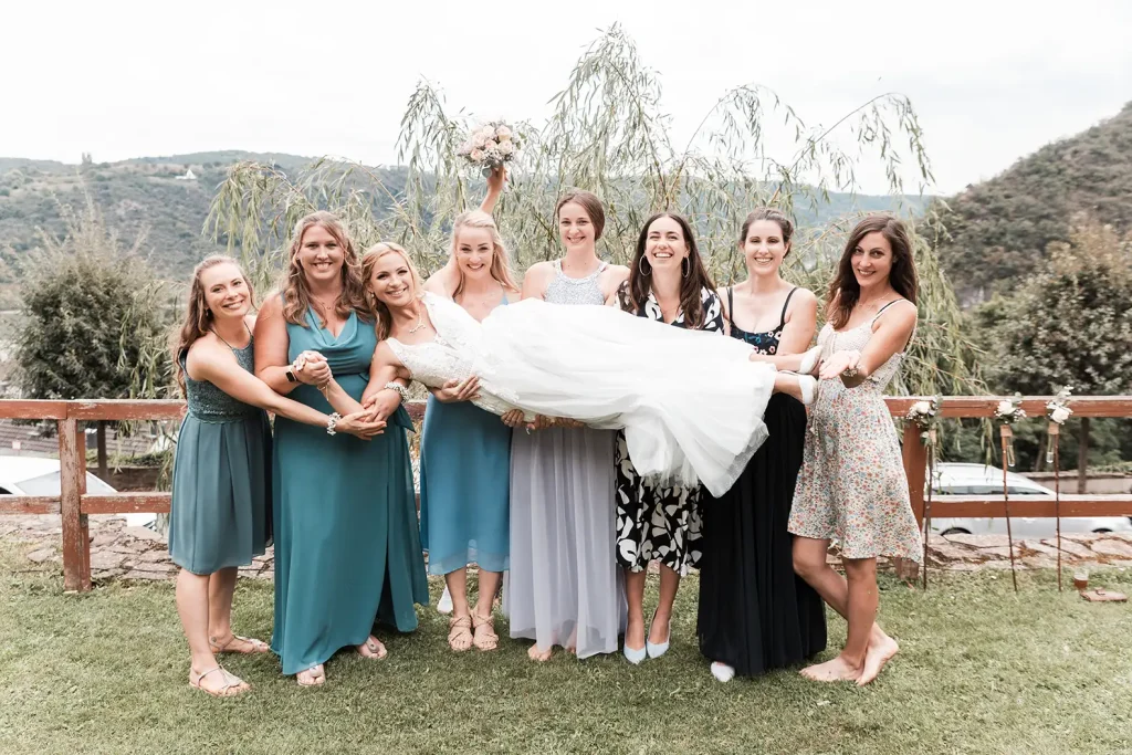 Braut wird von ihren Freundinnen bei einem fröhlichen Gruppenfoto während der Hochzeit getragen
