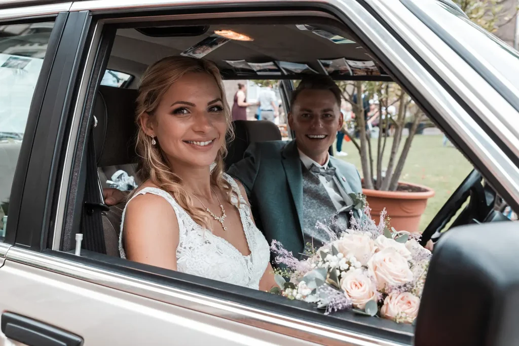 Brautpaar sitzt nach der Trauung mit Brautstrauß im klassischen Hochzeitsauto