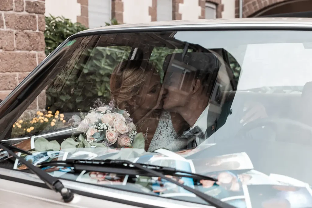 Brautpaar küsst sich im Hochzeitsauto hinter der mit Erinnerungsfotos dekorierten Windschutzscheibe