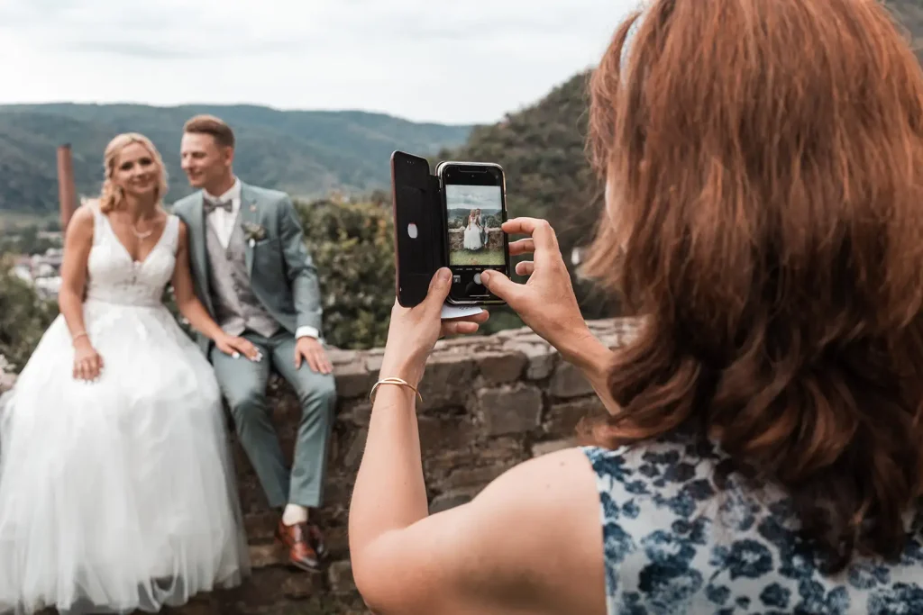 Hochzeitsgast fotografiert das Brautpaar vor der Landschaft rund um Schloss Burgbrohl
