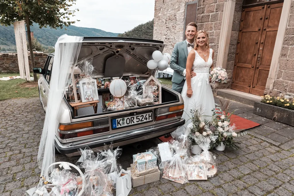 Brautpaar mit Hochzeitsgeschenken am als Überraschung dekorierten Hochzeitsauto vor Schloss Burgbrohl